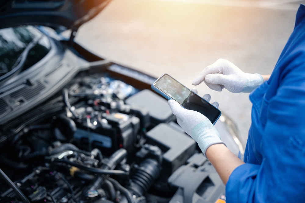 Mechanic,Examining,Car,Engine,With,Mobile,Phone,At,Auto,Repair